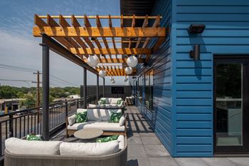A wooden pergola on a balcony with white couches and green pillows